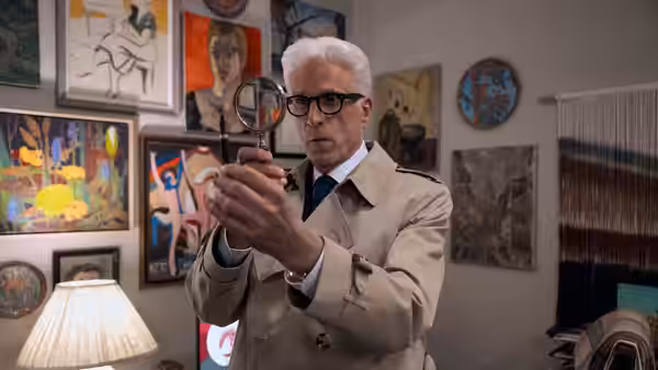 Charles Nieuwendyk (Ted Danson) examines artwork through a magnifying glass in a gallery