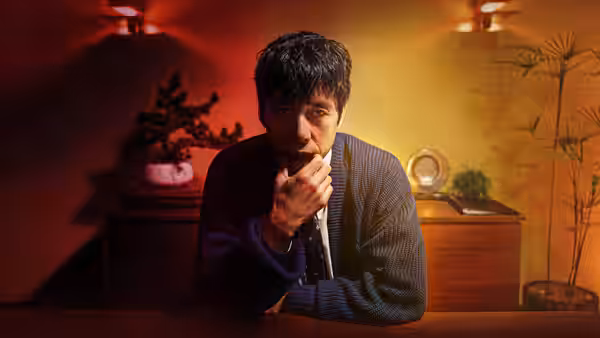 Masa (Hidetoshi Nishijima) leans forward thoughtfully in a warmly lit room