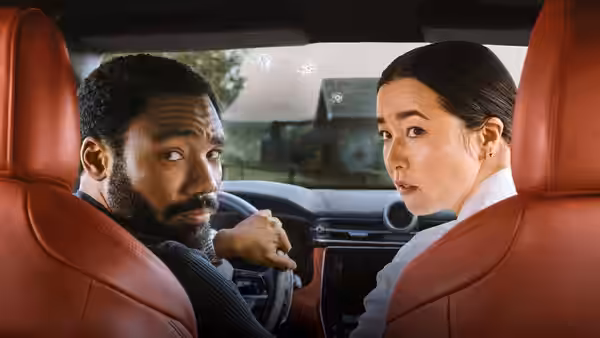 John Smith (Donald Glover) and Jane Smith (Maya Erskine) look back from the front seats of a car
