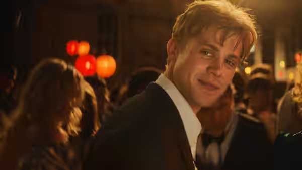 Dexter (Leo Woodall) turns toward the camera at a crowded party