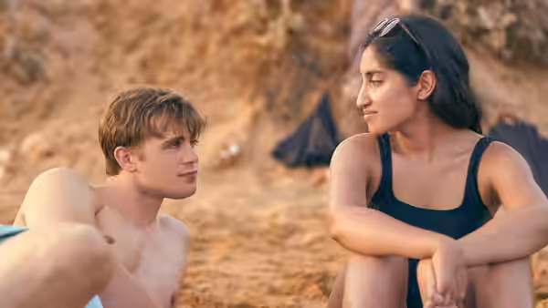 Emma (Ambika Mod) and Dexter (Leo Woodall) sit together on a beach