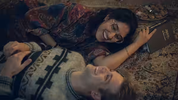 Emma (Ambika Mod) and Dexter (Leo Woodall) lie laughing on a patterned rug