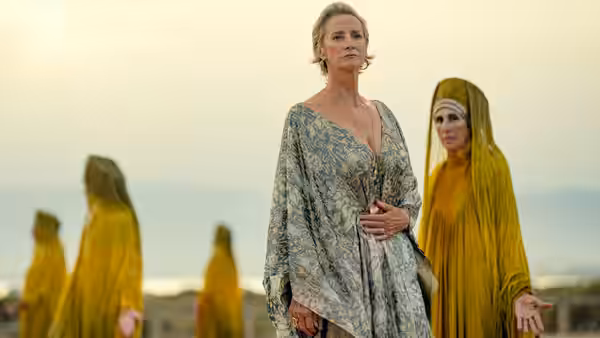 Hera (Janet McTeer) stands among yellow-veiled women on a coastal shore
