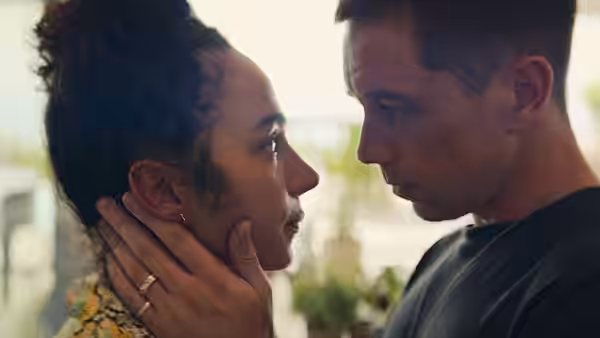 A man cups a woman’s face as they gaze at each other indoors