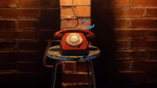 A red rotary telephone rests on a small stool against a brick wall