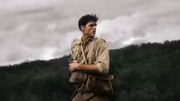 Dorrigo Evans (Jacob Elordi) in khaki uniform carrying a pack across a wooded hillside