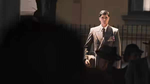 Dorrigo Evans (Jacob Elordi) stands in a decorated suit holding his hat before a seated crowd
