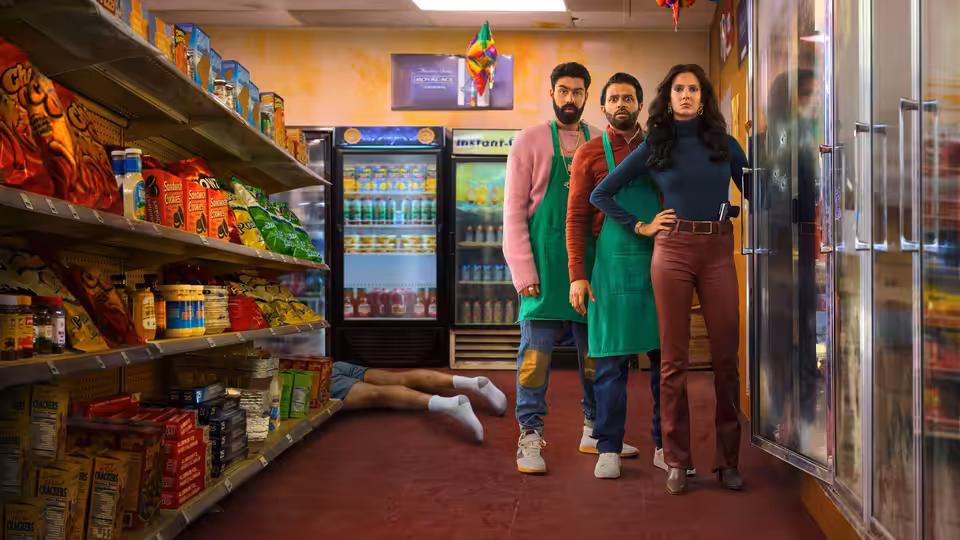 Lucky stands with Mir and Raj in the grocery aisle beside a body on the floor