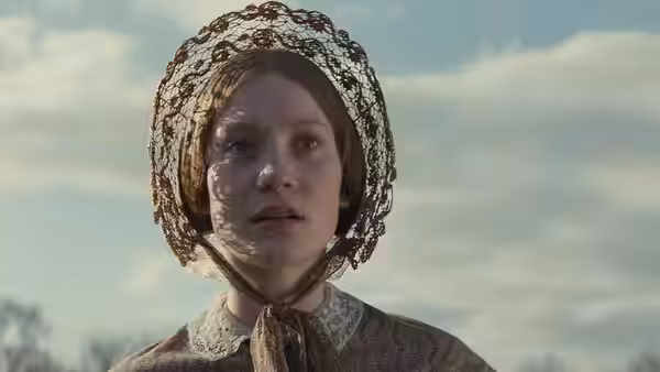 Jane Eyre (Mia Wasikowska) wears a lace bonnet beneath an open sky