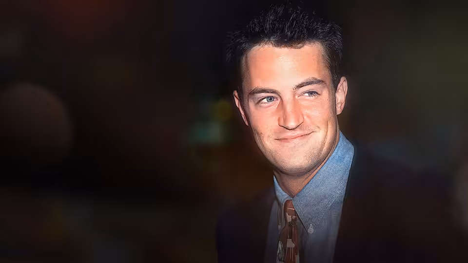 Matthew Perry smiling in a suit, glancing to the side