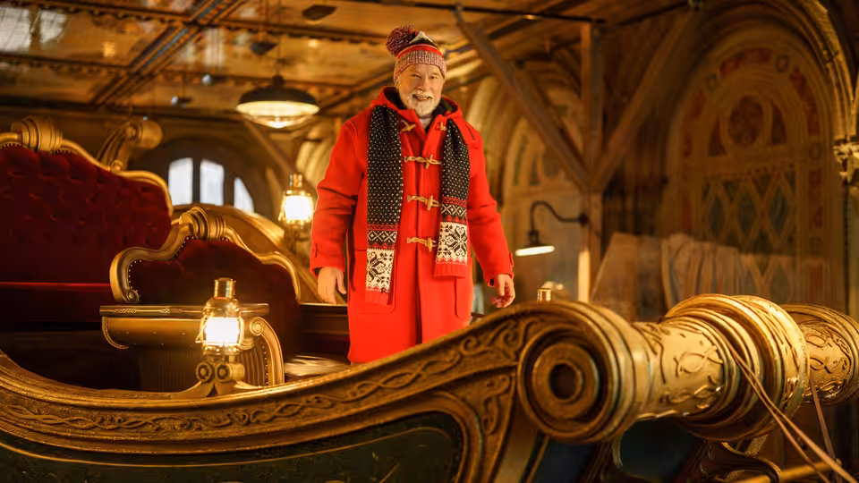 Santa (Arnold Schwarzenegger) stands aboard an ornate sleigh inside a warmly lit hall