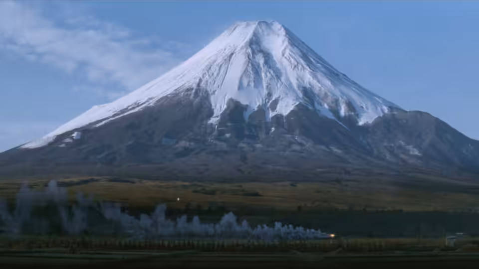 Mount Fuji rises above a dark shoreline and calm water