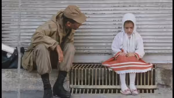 A uniformed soldier crouches beside Razieh (Aida Mohammadkhani), seated by a shutter