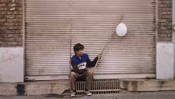 Ali (Mohsen Kafili) sits by a shutter, holding a pole with a white balloon