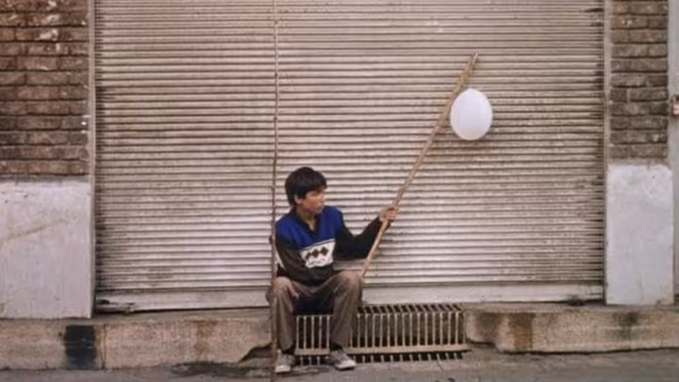 Ali (Mohsen Kafili) sits by a shutter, holding a pole with a white balloon