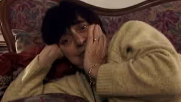 Agnès Varda lies on a floral sofa with her hands against her face