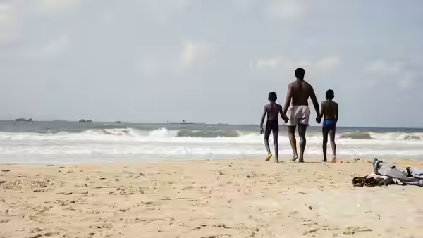 A man and two boys walk on a beach toward the sea