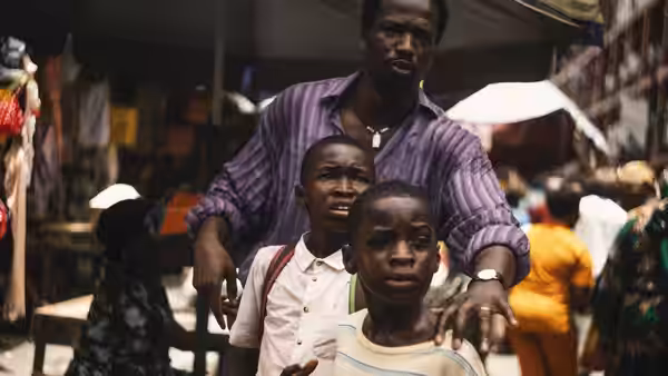 A man stands with two boys in a crowded outdoor market