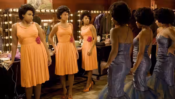 The Dreamettes compare their orange dresses with shimmering gowns in a dressing room