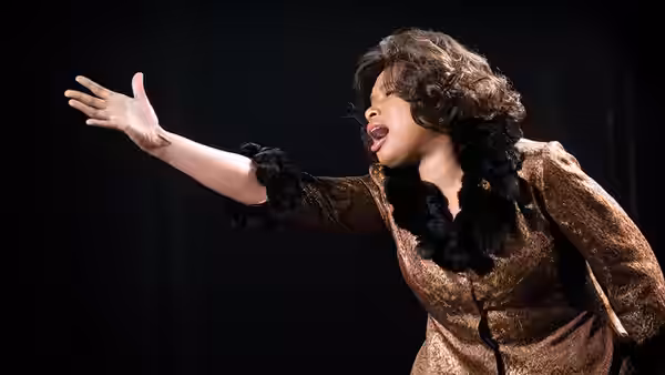 Effie White reaches out while singing in a brown fur-trimmed outfit