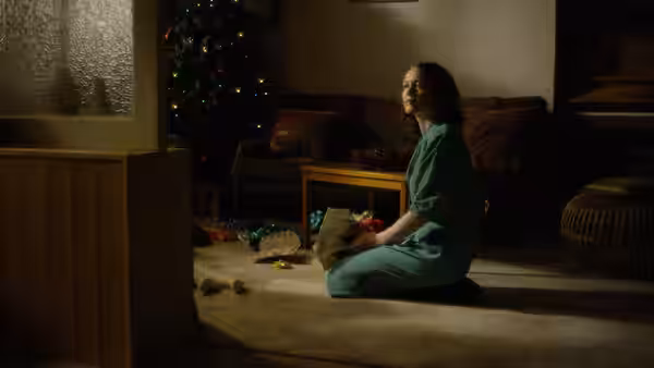A woman in a teal dress kneels beside scattered toys near a Christmas tree