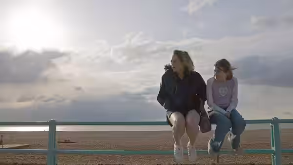 Kelly (Lorraine Stanley) and Joanne (Georgia Groome) sit on a seafront railing overlooking the beach