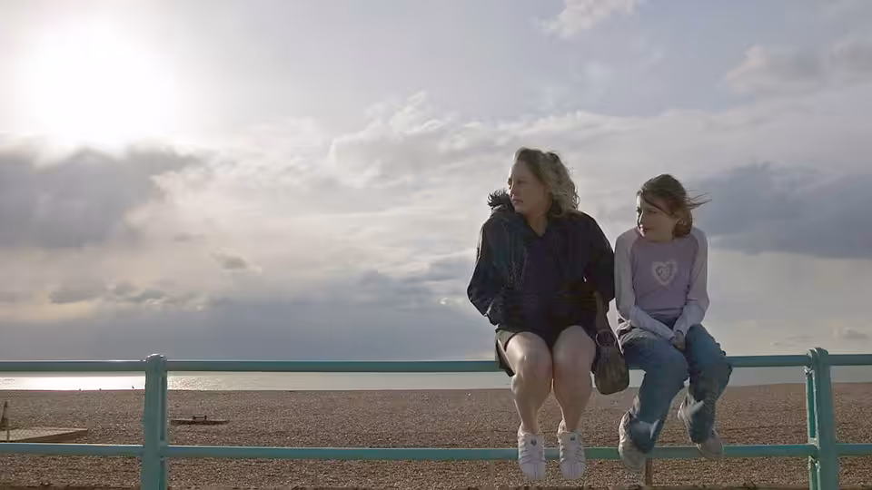 Kelly (Lorraine Stanley) and Joanne (Georgia Groome) sit on a seafront railing overlooking the beach