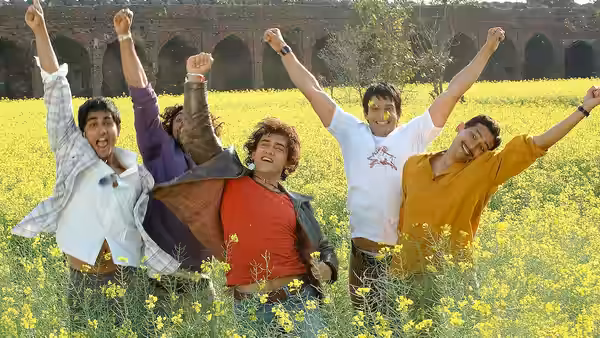 A group of young men cheer with raised arms in a mustard field before an old stone arcade