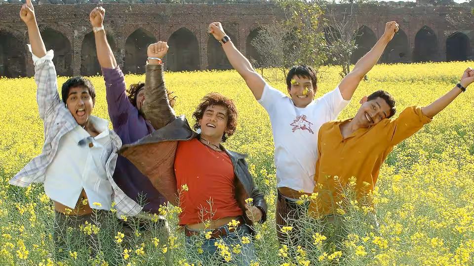 A group of young men cheer with raised arms in a mustard field before an old stone arcade