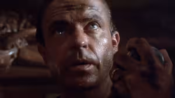 A sweaty man lies in darkness, gripping an object beside his face