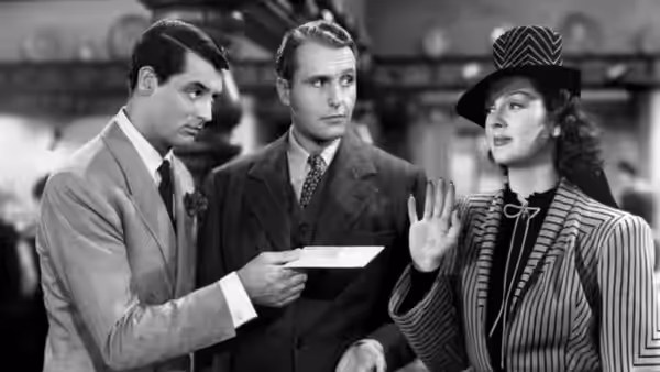 Hildy Johnson (Rosalind Russell) raising her hand while two men examine a paper