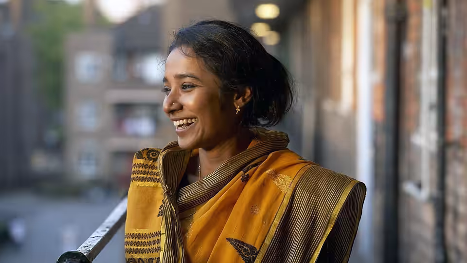 Nazneen (Tannishtha Chatterjee) smiles beside a window in her yellow sari
