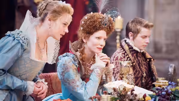 Elizabeth I (Cate Blanchett) sits at a banquet table beside a woman and young man