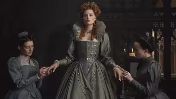 Queen Elizabeth I (Margot Robbie) stands as attendants adjust her gown