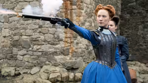 Mary Stuart (Saoirse Ronan) fires a pistol in a stone courtyard