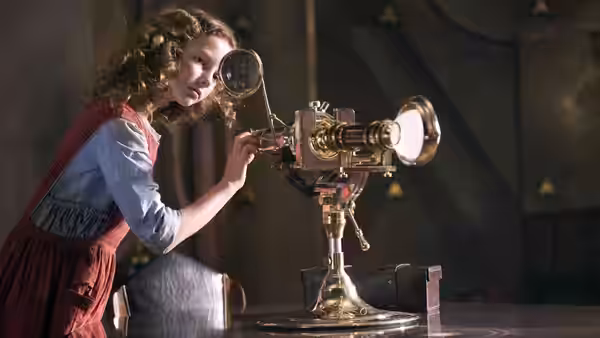 Lyra Belacqua (Dakota Blue Richards) peers through a brass optical instrument in a dim room