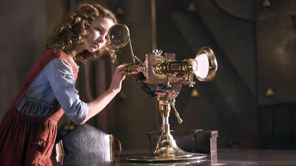 Lyra Belacqua (Dakota Blue Richards) peers through a brass optical instrument in a dim room