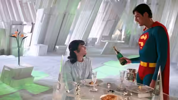 Superman (Christopher Reeve) offers Lois Lane (Margot Kidder) a bottle at a table in the Fortress of Solitude