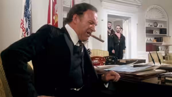 A cigar-smoking official leans over his desk as two men stand in the doorway