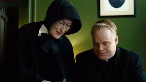 Sister Aloysius (Meryl Streep) leans over Father Flynn (Philip Seymour Hoffman) as he reads