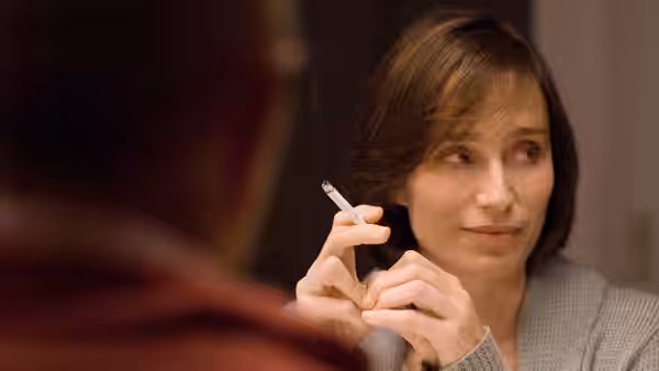 Léa (Elsa Zylberstein) holds a cigarette while looking across a table