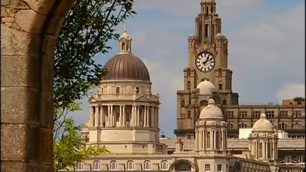 Domed civic buildings and a clock tower rise behind a stone archway