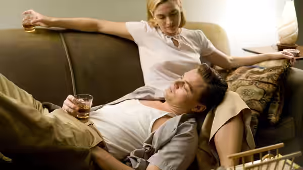April Wheeler sits on a sofa as Frank reclines beside her, both holding drinks