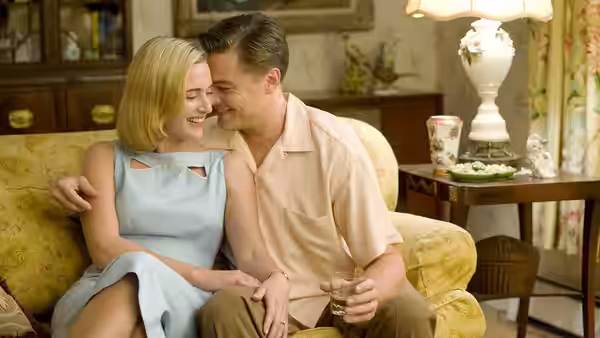 Frank and April Wheeler sit embracing on a living-room sofa