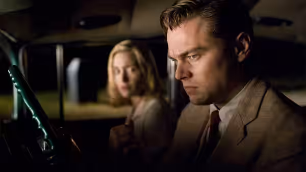 Frank Wheeler (Leonardo DiCaprio) sits tensely behind the wheel while April watches from the passenger seat