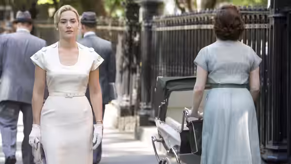 April Wheeler (Kate Winslet) walks along a city sidewalk as another woman pushes a stroller