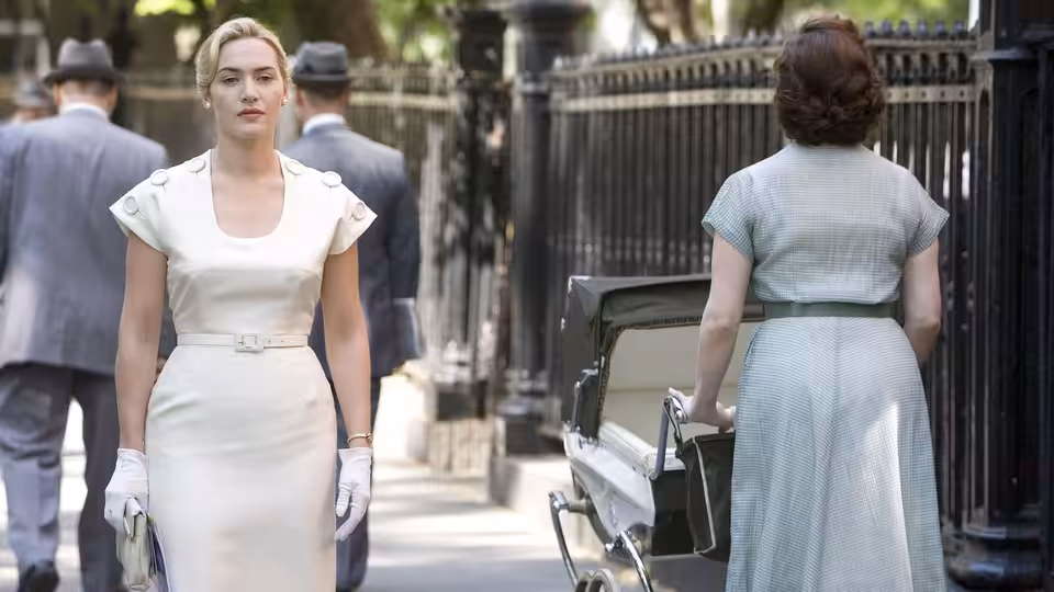 April Wheeler (Kate Winslet) walks along a city sidewalk as another woman pushes a stroller