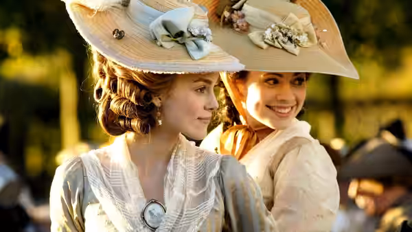 Georgiana Cavendish (Keira Knightley) and Bess Foster (Hayley Atwell) smile together outdoors in elaborate hats