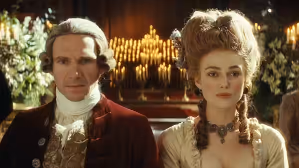Georgiana Cavendish (Keira Knightley) sits beside a powdered-wigged man in a candlelit room