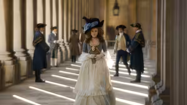 A woman in a white dress and blue hat walks beneath a colonnade as men watch